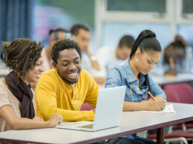 A multi-ethnic group of college age students surfing the web and researching a paper together.